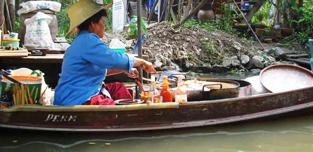 Thai vendor preparing authentic food in boat with conical hat - representing traditional timing and preparation